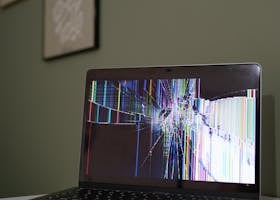 A laptop with a cracked and malfunctioning screen displayed on a desk indoors.