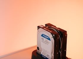 Dual external hard drives on a docking station with an orange backdrop.