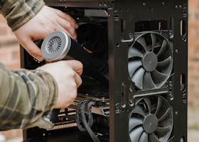 Hands cleaning a desktop PC case with an electric duster outdoors.